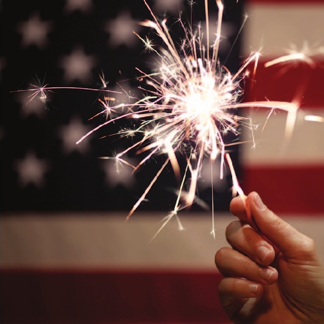a hand holding a sparkler in front of a flag
