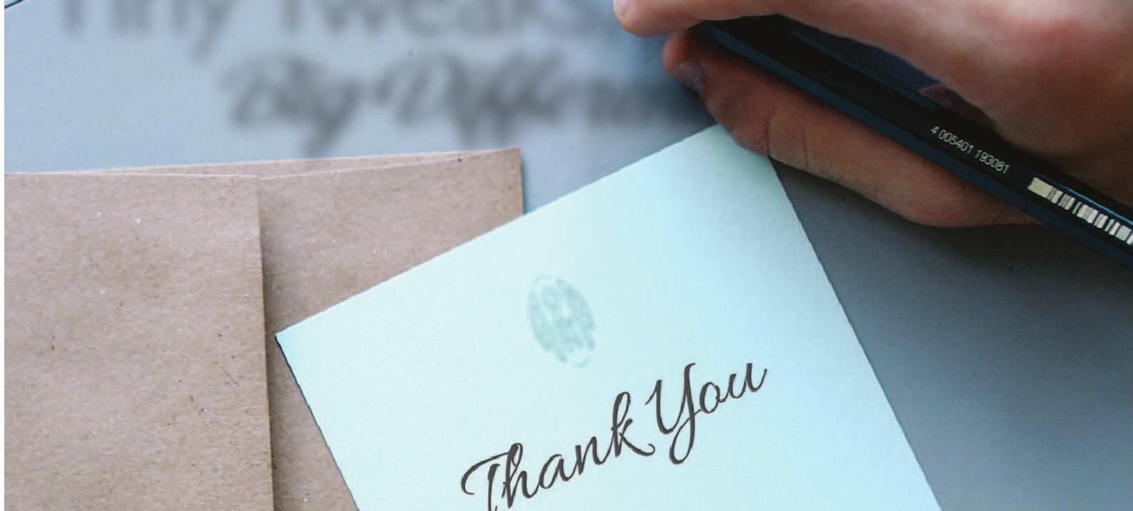 a hand holding a pen over a thank you card